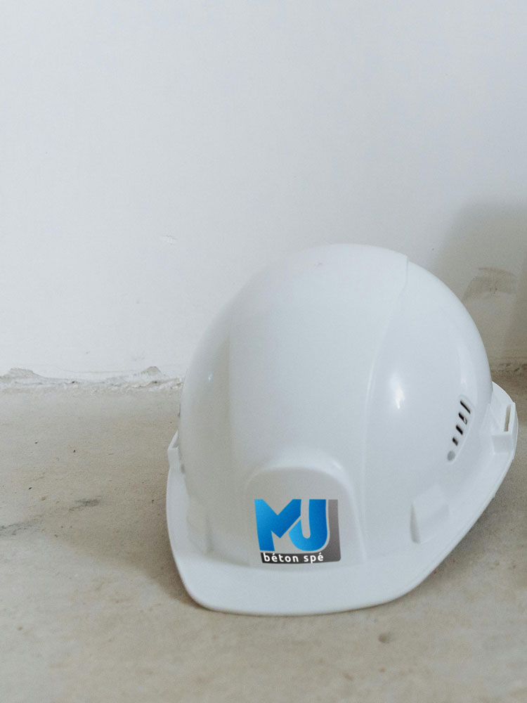 A construction helmet is lying on the ground, figuring MJ béton spé logo on it
