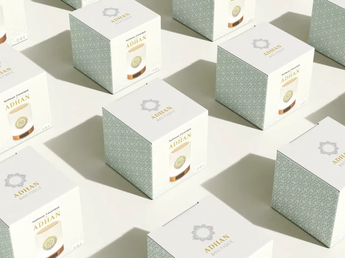 Vue en plongée d'une série de boîtes de packaging pour la veilleuse coranique ADHAN, avec motifs géométriques orientaux et logo doré.