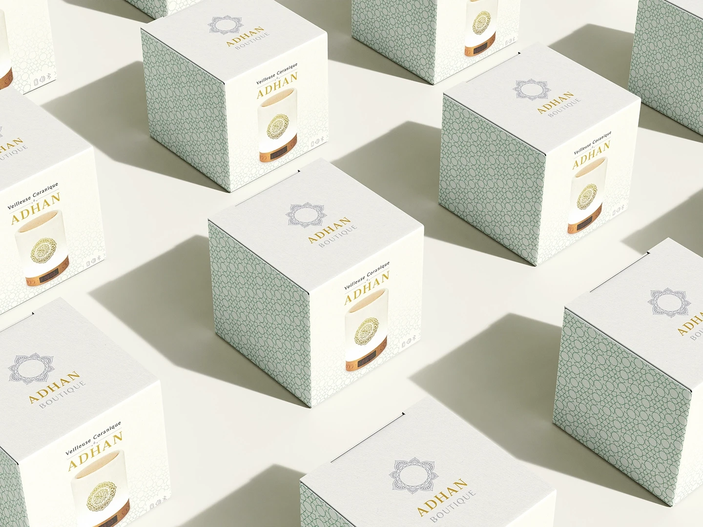Vue en plongée d'une série de boîtes de packaging pour la veilleuse coranique ADHAN, avec motifs géométriques orientaux et logo doré.