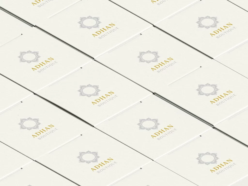 Répétition de logos dorés ADHAN Boutique sur le dessus de boîtes de packaging premium, design minimaliste et élégant.
